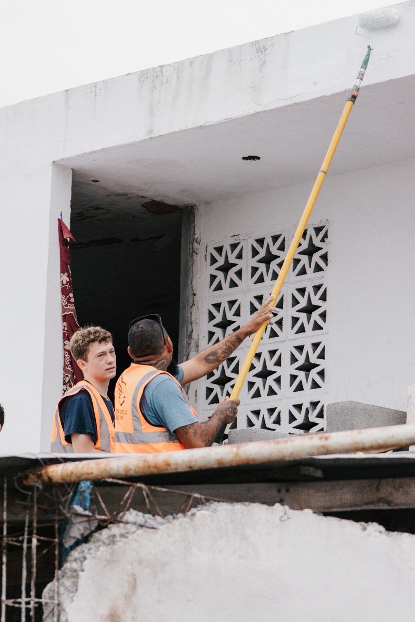 Two volunteers painting the upper floor of a home under repair