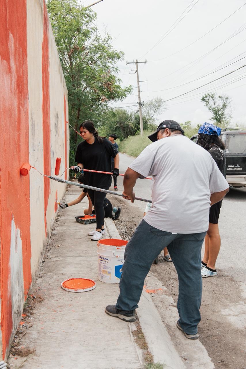 Volunteers rolling fresh orange paint onto a long neighborhood wall