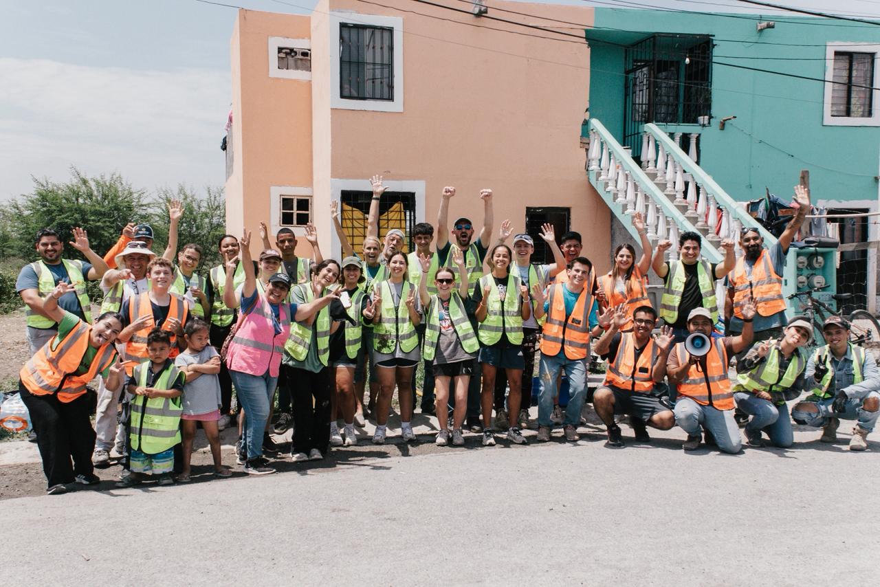 A large team of volunteers in safety vests cheering together in front of homes after a day of neighborhood work
