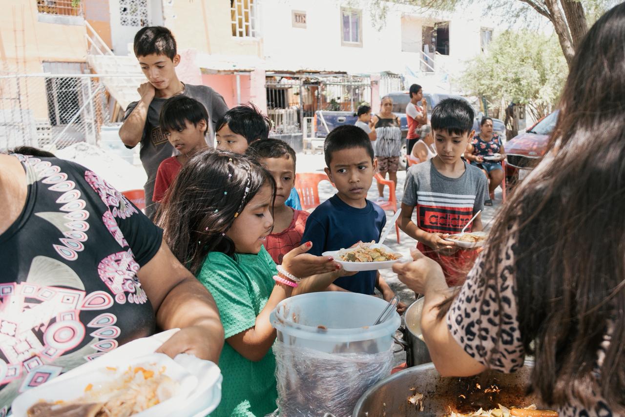 Children receiving plates of food at an outdoor neighborhood meal