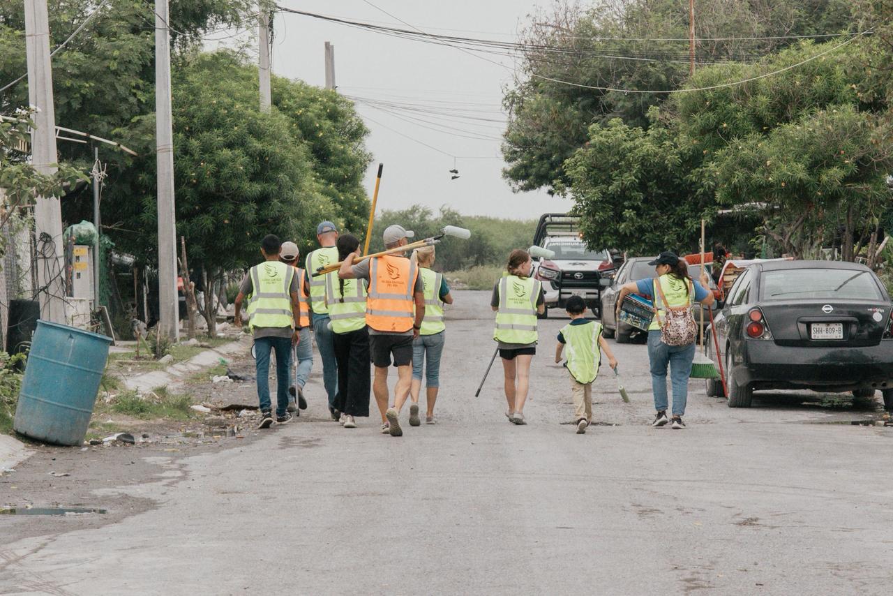 A crew of volunteers walking down a neighborhood street carrying brooms, shovels and paint rollers